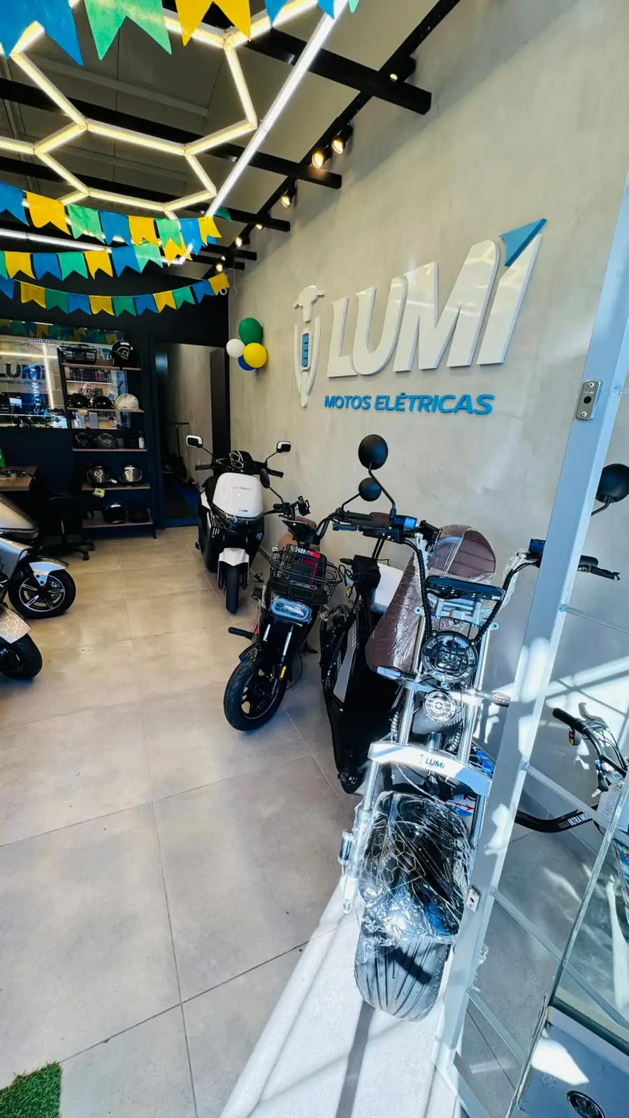 Parede do showroom com o logotipo da LUMI e veículos elétricos em exposição
